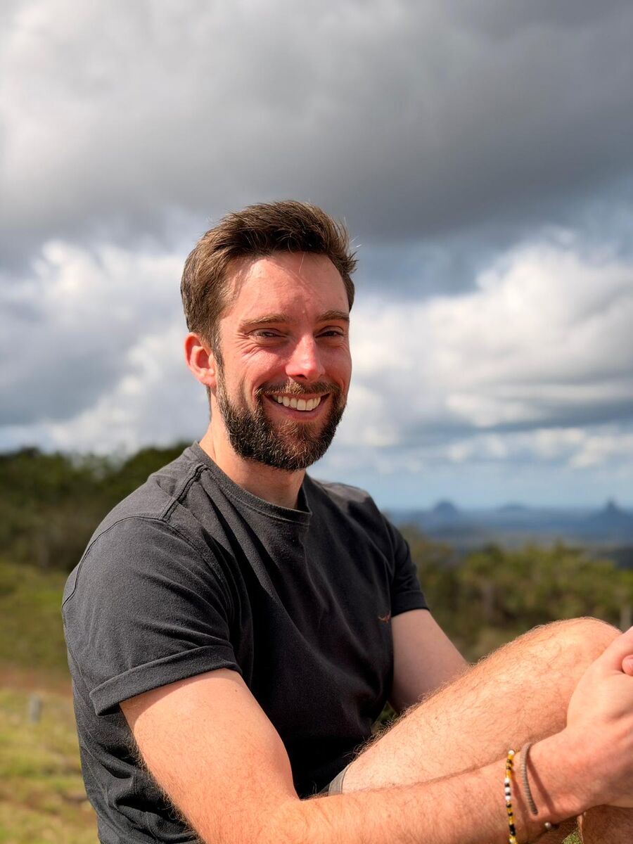 Josh smiling outdoors with the Glass House Mountains behind him