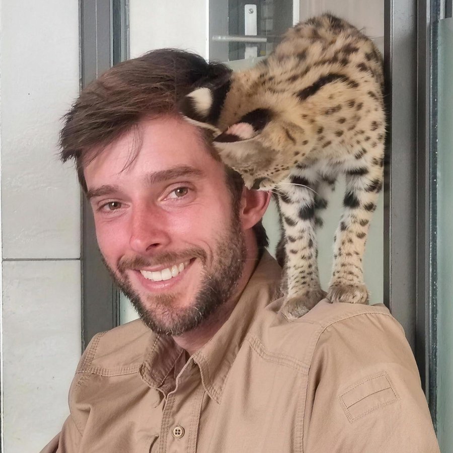 Joshua Rohl smiling, with a serval perched on his shoulder